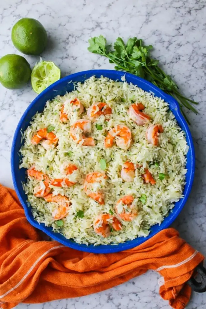 Cilantro Lime Shrimp & Rice served in a blue pan with fluffy herb rice, cooked shrimp, fresh cilantro, and whole limes on marble background