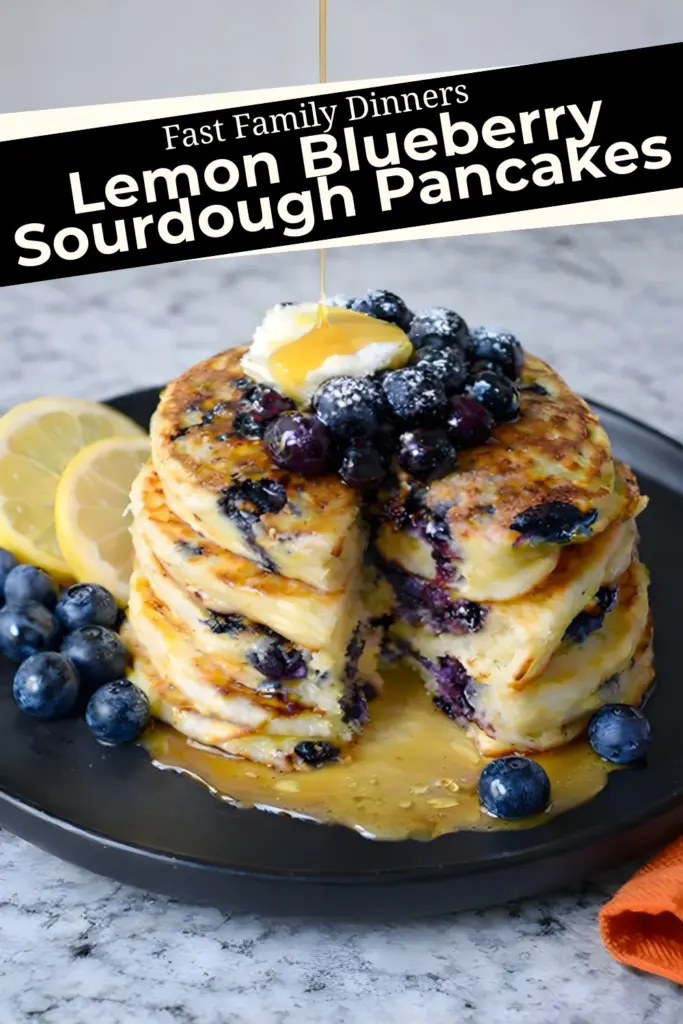 Lemon blueberry sourdough pancakes with syrup, butter, and fresh blueberries on black plate
