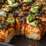 Spicy salmon sushi bake with avocado slices, green onions, sesame seeds, and nori in baking dish