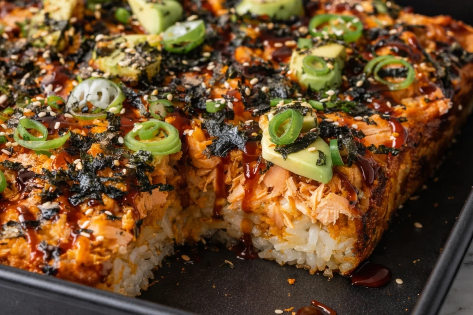 Spicy salmon sushi bake with avocado slices, green onions, sesame seeds, and nori in baking dish