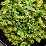 Spring pea pesto pasta with rotini, fresh peas, herbs, and creamy green pesto in a black bowl