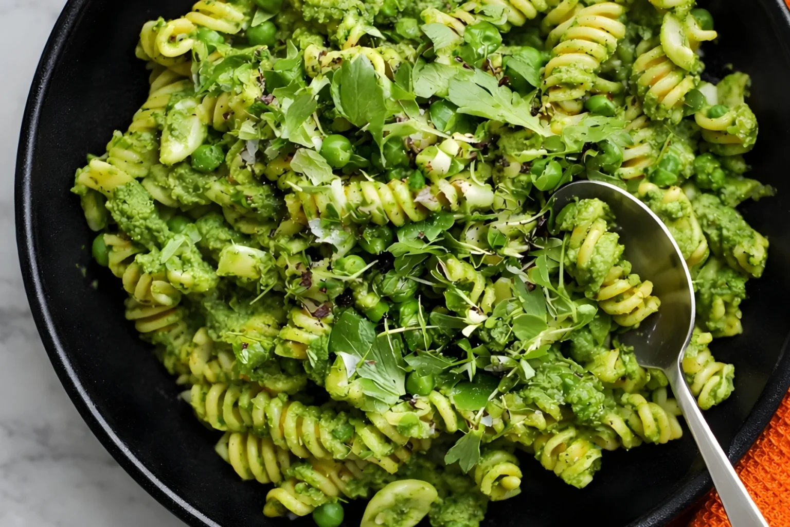 Spring pea pesto pasta with rotini, fresh peas, herbs, and creamy green pesto in a black bowl