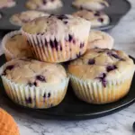 Sourdough discard blueberry lemon muffins stacked on black plate with fresh blueberries and lemon