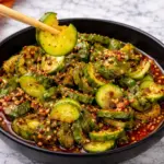 Korean cucumber salad with spicy sauce in black bowl on marble countertop