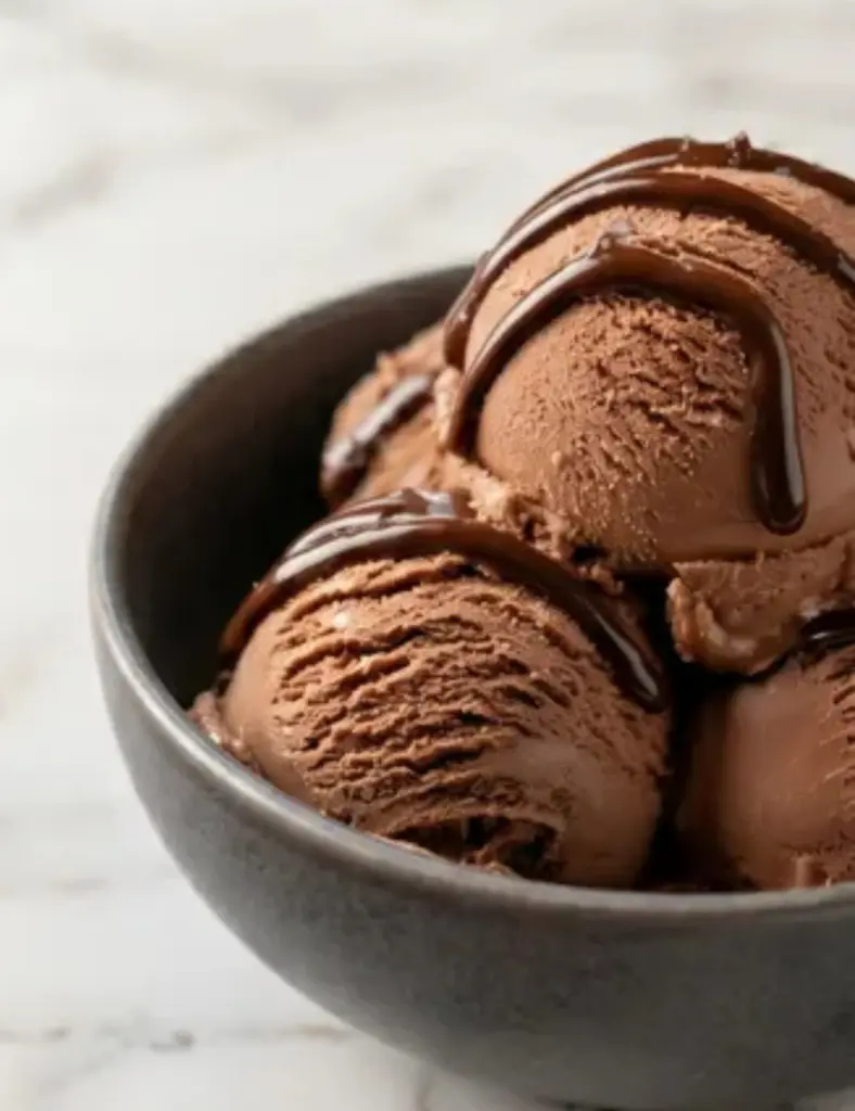 close up of cottage cheese chocolate ice cream scoops with chocolate drizzle in a dark bowl on marble surface