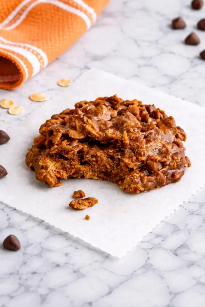bite taken no bake peanut butter cookie with chocolate oats on parchment paper marble countertop