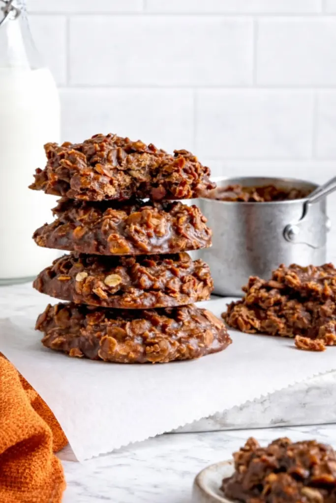 No bake peanut butter cookies stacked on parchment paper with chocolate oats on marble countertop