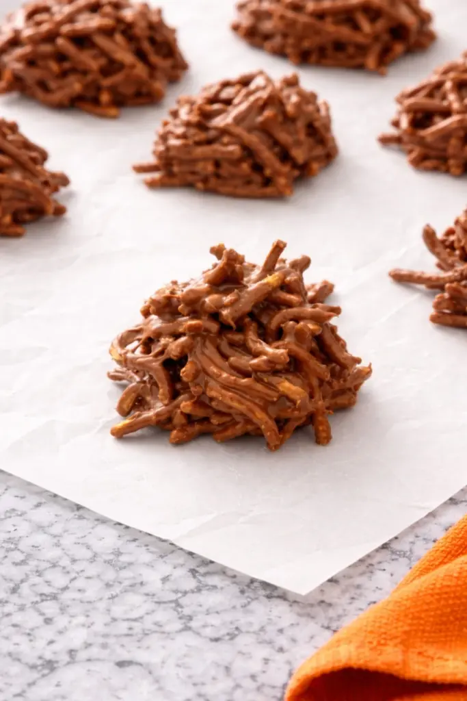 Chocolate haystack cookies on parchment paper over marble countertop with orange towel