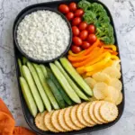 Cottage cheese ranch dip served with fresh veggies, crackers and chips on a black platter over a marble kitchen countertop