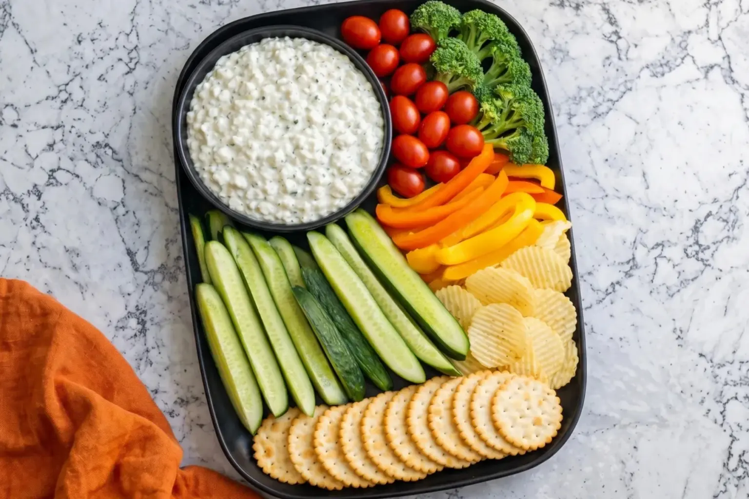 Cottage cheese ranch dip served with fresh veggies, crackers and chips on a black platter over a marble kitchen countertop