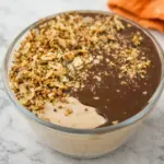Chocolate peanut butter cottage cheese breakfast bowl topped with granola and smooth chocolate sauce in a glass bowl on a marble countertop