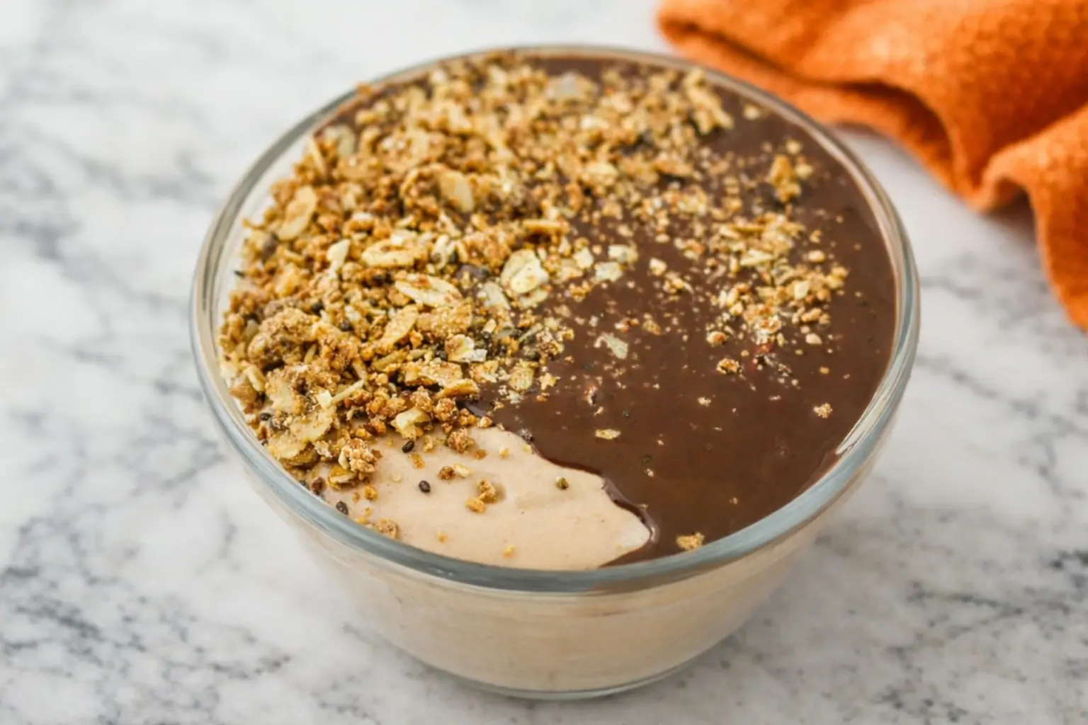 Chocolate peanut butter cottage cheese breakfast bowl topped with granola and smooth chocolate sauce in a glass bowl on a marble countertop