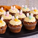 Easter carrot cake cupcakes with cream cheese frosting and bunny toppers on black tray