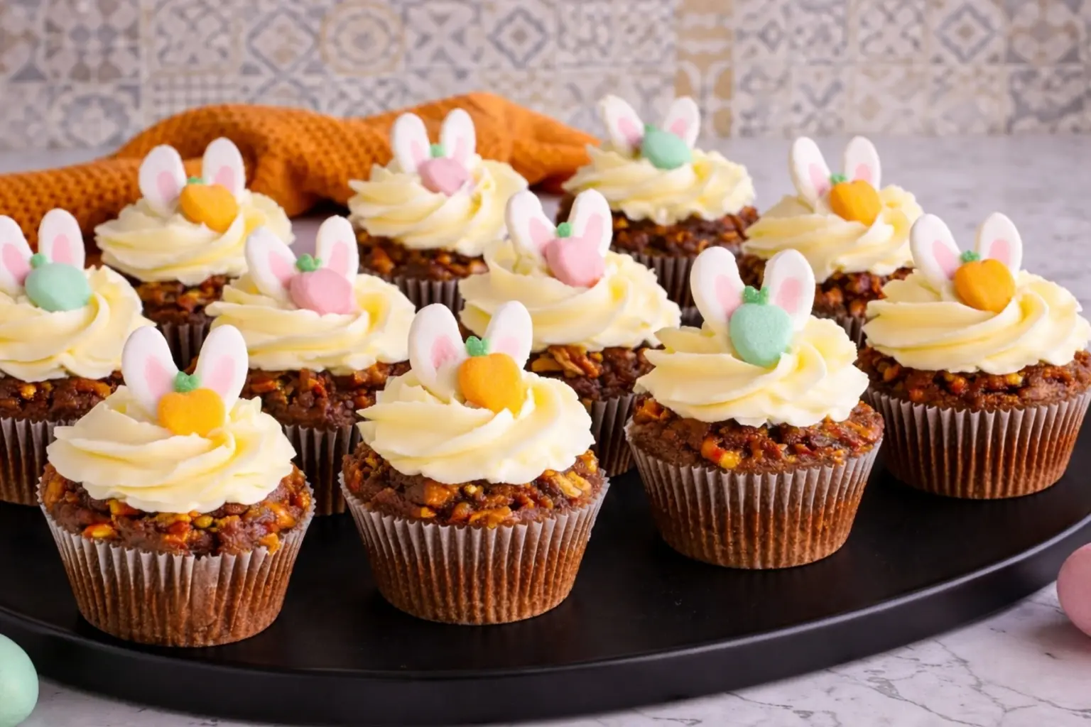 Easter carrot cake cupcakes with cream cheese frosting and bunny toppers on black tray