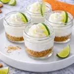 No-bake key lime pie jars with creamy cheesecake layers, graham cracker crust, whipped cream, and fresh lime wedges on a marble tray