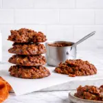 No bake peanut butter cookies stacked on marble countertop with parchment paper and orange kitchen towel