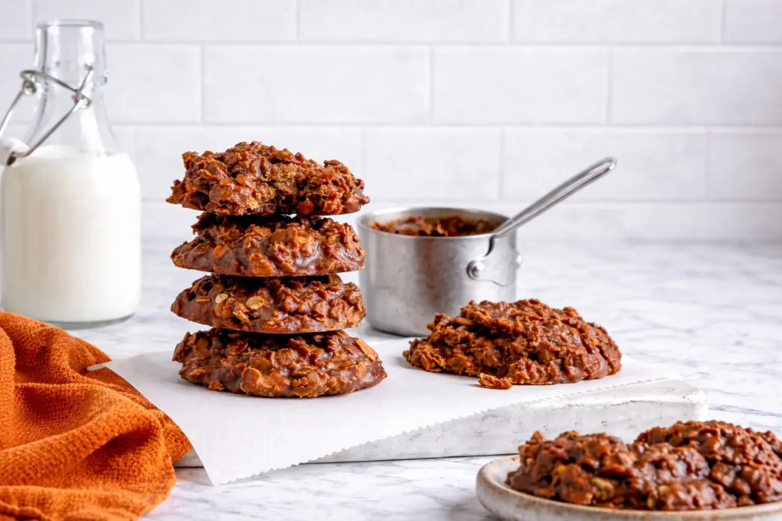 No bake peanut butter cookies stacked on marble countertop with parchment paper and orange kitchen towel