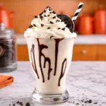 Cookies and Cream Milkshake in a tall glass with whipped cream and chocolate drizzle