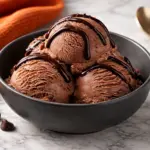 Cottage cheese chocolate ice cream in a dark gray bowl topped with chocolate drizzle on a marble countertop with an orange kitchen towel