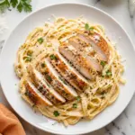 Chicken Alfredo Recipe with creamy fettuccine, sliced golden chicken, parmesan, and parsley served on a white plate.