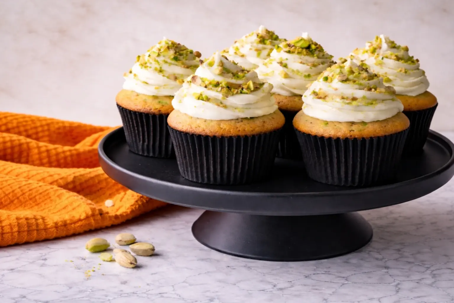 Pistachio cupcakes with creamy frosting on black cake stand