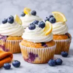 Lemon blueberry cupcakes with cream frosting and fresh blueberries on marble countertop
