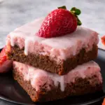 Fudgy strawberry brownies with pink icing on black plate