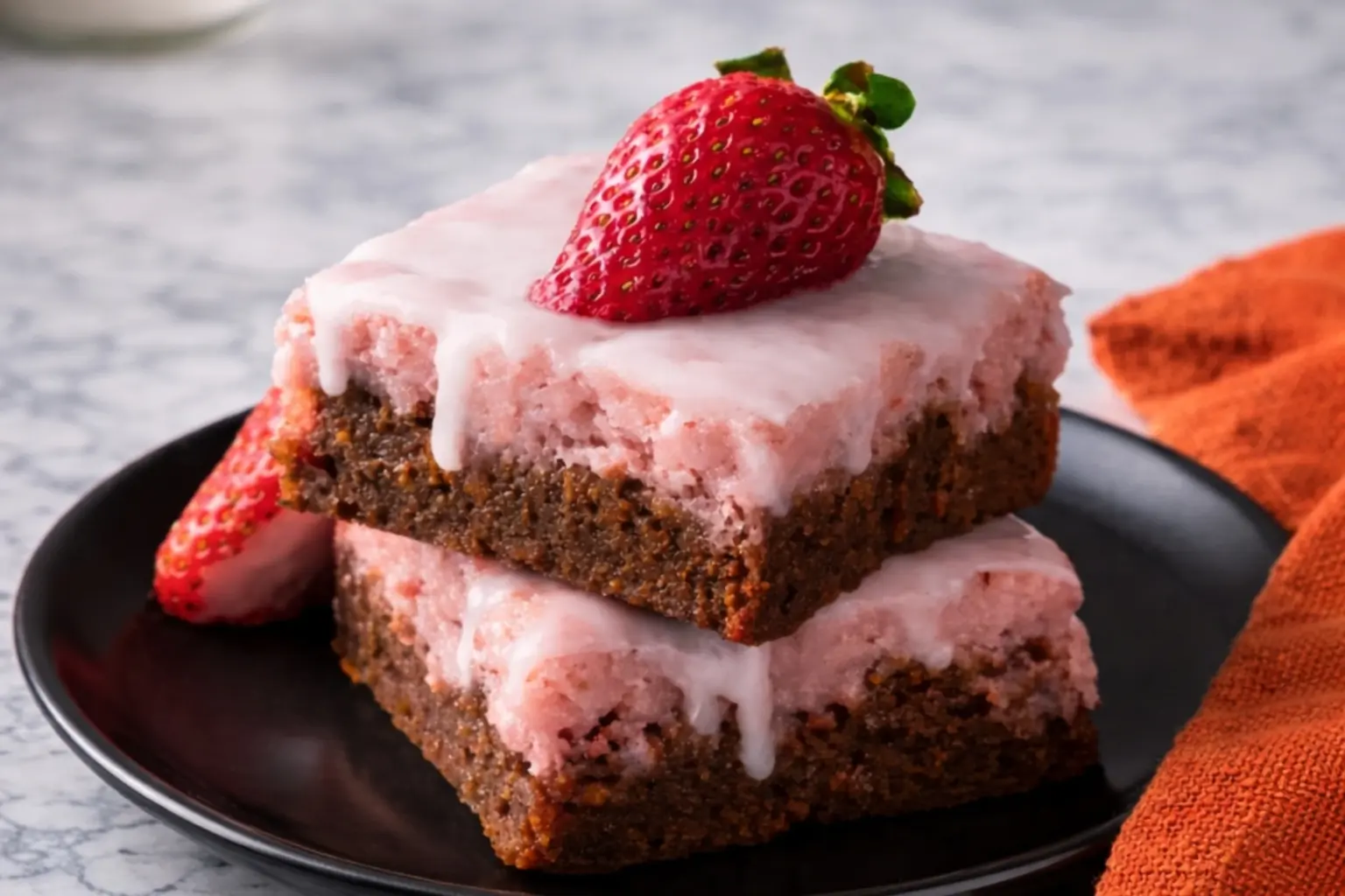 Fudgy strawberry brownies with pink icing on black plate