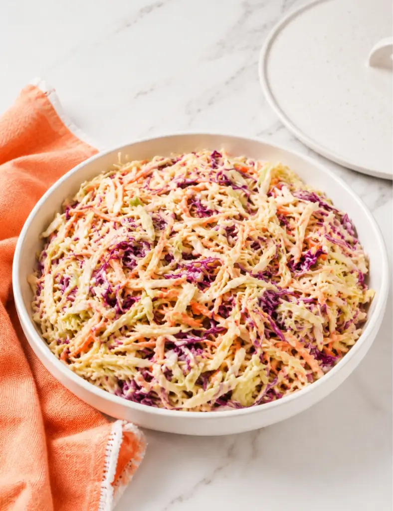 Creamy Coleslaw Recipe served in a white bowl with shredded cabbage, carrots, and a creamy mayonnaise dressing on a marble countertop.
