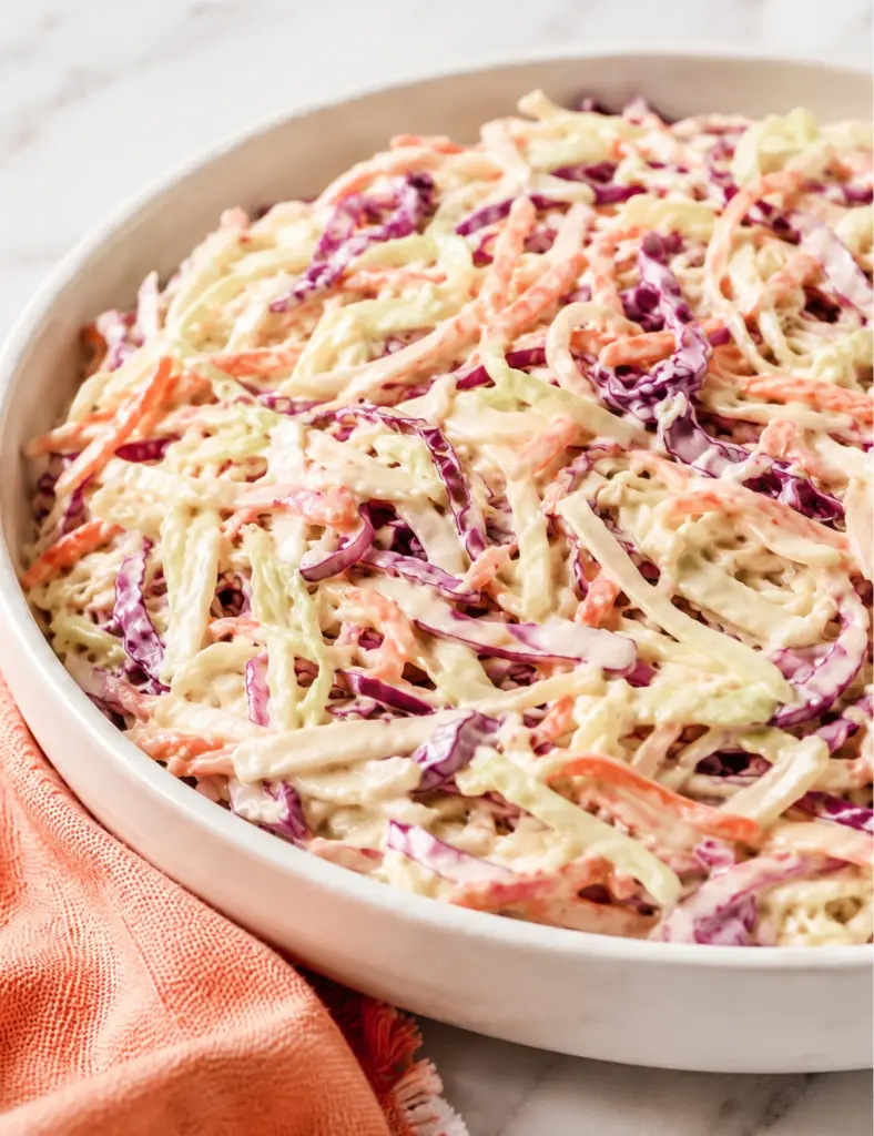 Close-up of a creamy coleslaw recipe in a white serving bowl with shredded green cabbage, red cabbage, carrots, and a glossy mayonnaise dressing.