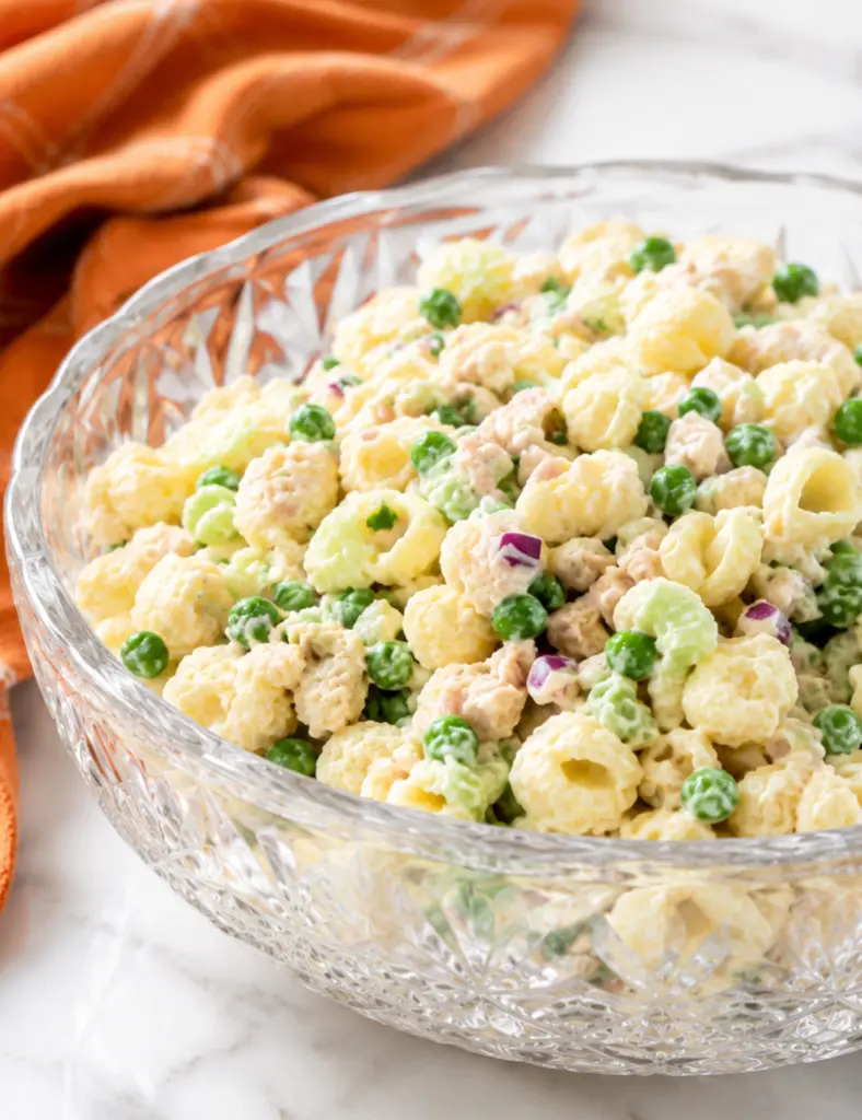 Creamy tuna pasta salad with shell pasta, peas, celery, red onion, and tuna served in a crystal bowl on a white marble countertop.