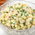 Creamy tuna pasta salad with shell pasta, peas, celery, red onion, and tuna in a crystal serving bowl on a marble countertop.