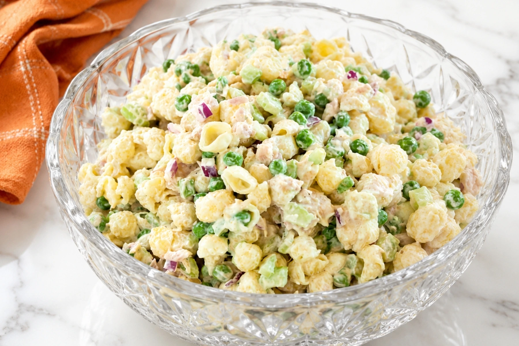 Creamy tuna pasta salad with shell pasta, peas, celery, red onion, and tuna in a crystal serving bowl on a marble countertop.