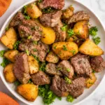 Blackstone Steak and Potatoes with juicy steak bites, golden potatoes, fresh parsley, and garlic butter served in a white bowl on a marble countertop.