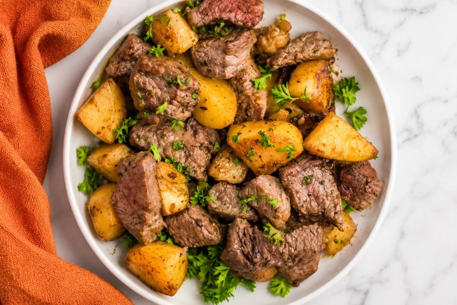 Blackstone Steak and Potatoes with juicy steak bites, golden potatoes, fresh parsley, and garlic butter served in a white bowl on a marble countertop.