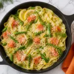 Smoked Salmon Pasta with creamy fettuccine, asparagus, lemon slices, fresh dill, and parmesan in a black skillet on a white marble countertop.