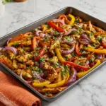 Sheet Pan Chicken Fajitas with sliced chicken, bell peppers, red onions, and fresh cilantro roasted in a sheet pan on a white marble countertop.