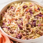 Creamy Coleslaw Recipe in a white serving bowl with shredded cabbage, carrots, red onion, and a creamy mayonnaise dressing on a marble countertop.