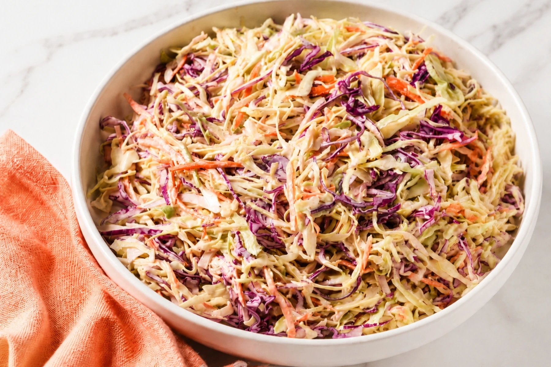 Creamy Coleslaw Recipe in a white serving bowl with shredded cabbage, carrots, red onion, and a creamy mayonnaise dressing on a marble countertop.