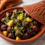 Slow Cooker Teriyaki Meatballs with pineapple, sesame seeds and sliced green onions served in a glazed terracotta dish on a white marble countertop.