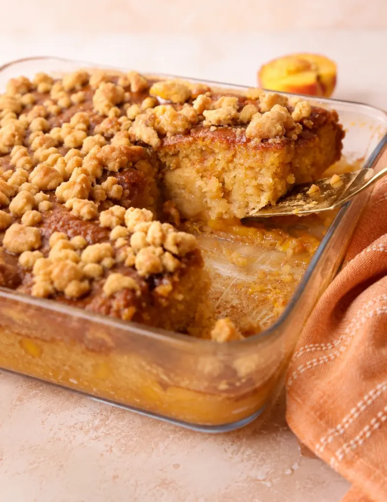 Peach Sticky Pudding in a glass baking dish with crumb topping and a warm gooey peach layer