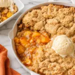 Cast Iron Skillet Peach Cobbler with juicy peach filling, golden crumble topping, vanilla ice cream, and a plated serving.