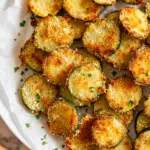 Crispy Zucchini Parmesan Crisps baked until golden brown, served on parchment paper with fresh parsley on a white plate.