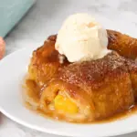 Peach Dumplings with Crescent Rolls topped with vanilla ice cream on a white plate